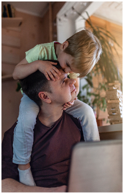 Father working on a laptop with kid on his back